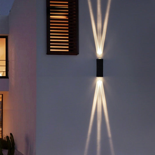 Wall-mounted outdoor light fixture casting a beam of light on a white wall.